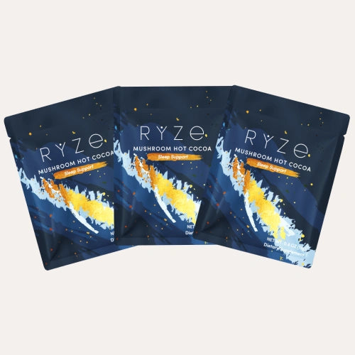 Three RYZE Mushroom Hot Cocoa single-serve sachets with navy abstract comet design fanned out on a cream background